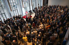 Viele Personen stehen im Festsaal und hören Antje Grotheer zu, die an einem erhöhten Rednerpult vor dem Fenster steht.