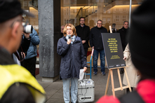 Antje Grotheer steht mit einem Mikro in der Hand vor den Zuhörern. Neben ihr ist eine Staffelei mit einer Infotafel zu sehen.