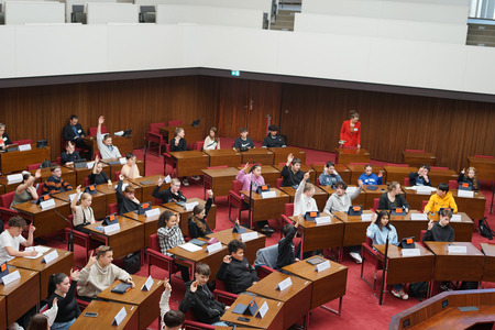 Schüler:innen sitzen im Plenarsaal, teilweise mit zur Abstimmung erhobenen Händen